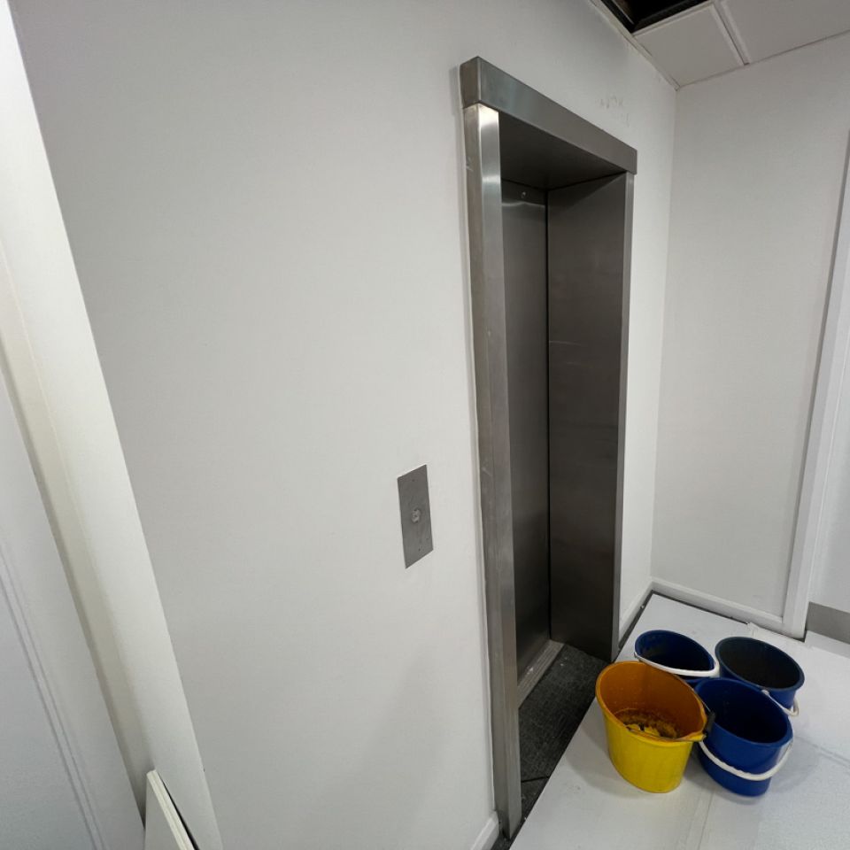 Open lift with buckets collecting water below, showing an active roof leak inside a commercial building.